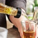 A person using a TableCraft yellow tail liquor pourer to pour liquid into a glass on a counter.