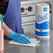 A person wearing blue gloves using a Scott 1-ply paper towel roll to clean a kitchen counter.