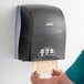 A person putting a piece of paper towel on a Kimberly-Clark Professional Sanitouch Manual Hard Roll Towel Dispenser.