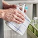 A hand cleaning a glass with a blue and white Monarch Brands terry dish cloth.