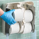 A hand wearing blue gloves holds a Scott Essential toilet paper roll.