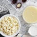 A bowl of Cacao Barry white chocolate pistoles next to a bowl of white liquid.