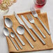 A close-up of Acopa Petra distressed stainless steel salad/dessert fork and knife on a table with a napkin and flowers.