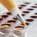 A pastry bag being used to fill chocolate cups with American Almond Hazelnut Paste.