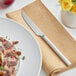 A plate of meat and mushrooms on a napkin next to an Acopa stainless steel steak knife.