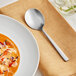 An Acopa stainless steel bouillon spoon in a bowl of soup.