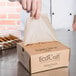 A hand putting Bagcraft Packaging EcoCraft Bakery Tissue in a box.