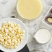 A bowl of Callebaut white chocolate chips on a marble counter.