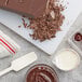 A Callebaut dark chocolate bar on a cutting board with a bowl of brown liquid and chocolate chips.