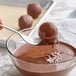 A fork dipping a chocolate ball in Cacao Barry Brune compound coating.