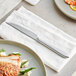 An Acopa Pangea steak knife on a napkin next to a plate of food.