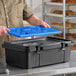 A black top-loading insulated food pan carrier with a blue ice board, designed to hold a full-size pan up to 6 inches deep.