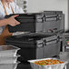 A woman using a CaterGator black food pan carrier to hold a stack of food containers.