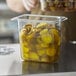 A person's hand holding a clear plastic container of pickles on a counter.