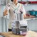 A woman in a white coat using a Robot Coupe CL50 food processor to cut onions.