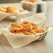 A close up of a basket of fried onion rings with a natural kraft EcoChoice deli liner inside.