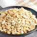 A bowl of raw cashew pieces on a table with a napkin.