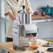 A woman using a Robot Coupe CL50 Ultra food processor to dice carrots.