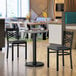 A 36-inch round reversible table with a white and gray slate laminated top, shown with two black chairs in a modern dining setting.