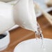 A white pitcher pouring water into a white porcelain sake bottle.