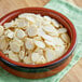 A bowl of blanched sliced almonds on a green cloth.