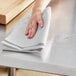 A hand holding a gray-striped herringbone kitchen towel over a table.