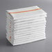 A stack of white herringbone kitchen towels with orange stripes.