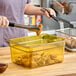A woman using tongs to place a chicken wing in a clear Cambro plastic food pan on a counter.