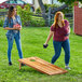 Two women playing cornhole with a Backyard Pro Courtyard Series rosewood cornhole set.