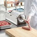 A person in a white coat and gloves using an Avantco stainless steel horizontal manual sausage stuffer on a counter.