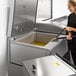 A woman using a VITO fryer oil filter to remove yellow oil from a fryer.