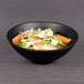 A bowl of food with broccoli, carrots, and noodles on a table.