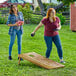 Two women playing a game of Backyard Pro rustic dark wood cornhole on grass.