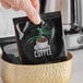 A hand holding a packet of Regular Room Service 4-Cup Coffee Filters in a bowl.