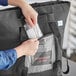 A person putting a plastic bag inside a Choice black insulated tote bag.