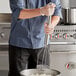 A man using a Tablecraft stainless steel potato masher to mash potatoes in a bowl.