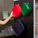 A woman's hand holding a green plastic container on a black Cambro pegboard.