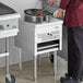 A man in a red shirt using a Cooking Performance Group natural gas Wok Range to cook food in a pan.