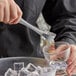 Choice stainless steel tongs holding ice over a glass cup.