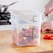 A person cutting tomatoes in a Vigor translucent square plastic container on a counter.