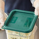 A person in gloves holding a Vigor translucent square polypropylene food storage container full of shredded cheese.
