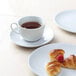 A white plate with a Tuxton Florence white china cup of tea and a croissant.