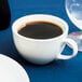 A Tuxton bright white china cup of coffee on a table.