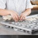 A person making dough in a Chicago Metallic clustered hot dog bun pan.