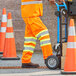A person wearing Ergodyne orange Class E pants with reflective stripes pushing a hand truck.