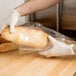 A gloved hand using an LK Packaging plastic food bag to hold a baguette.