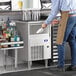 A man standing in front of a Manitowoc undercounter ice machine with a glass of ice.