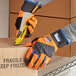 A person wearing Ergodyne ProFlex orange thermal waterproof work gloves cuts a box.