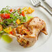 A plate of food with a whole quail, salad, and a fork and knife.