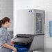 A woman in a grey shirt opening a Manitowoc air cooled nugget ice machine filled with ice.